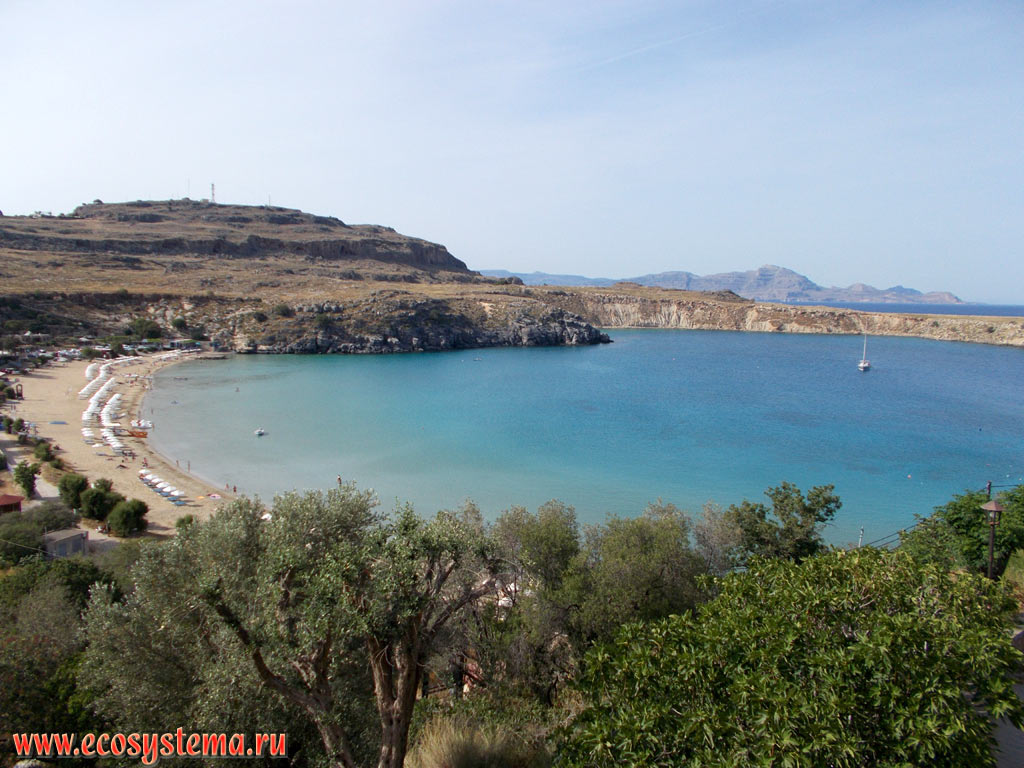 The Lindos Bay with a sandy beach on the South-Eastern (Mediterranean) coast of the island of Rhodes with medium-altitude mountains, composed of limestone