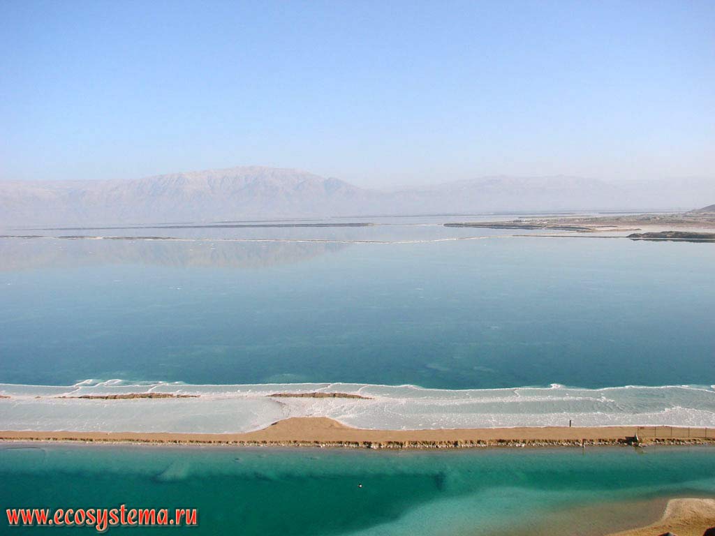 Мертвое море (бессточное соленое озеро) с печаным баром и лагуной (на переднем плане) и косами (вдали) и отложениями морской соли.
Дымка над озером - испарения брома. Азиатское Средиземноморье, или Левант, Мертвое море, Израиль