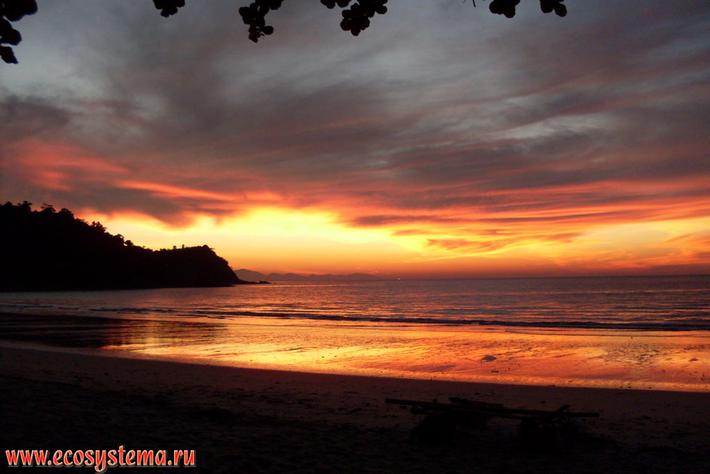 Beautiful maroon sunset in the Molae Bay (Ao Molae) on the coast of the Malacca Strait of Andaman Sea with the island of Langkawi (Indonesia) far away