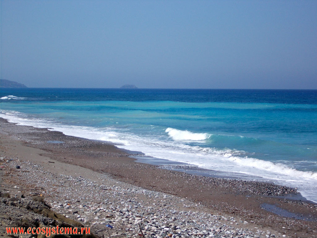 Surf on the sandy-pebble beach and the blue waters of the Aegean Sea on the West coast of Rhodes